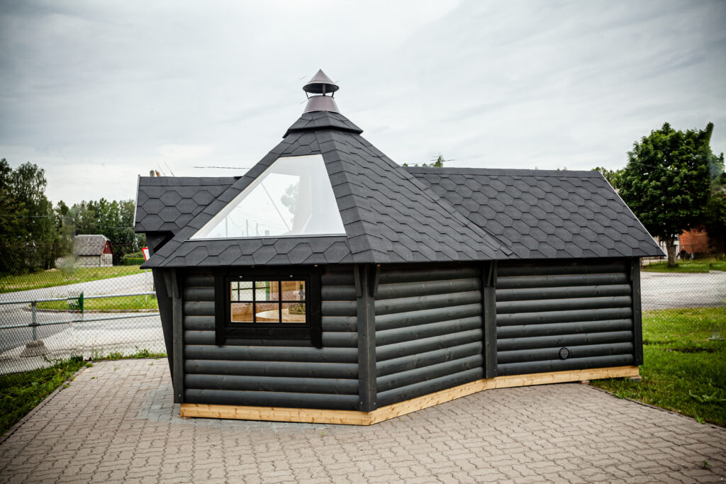 Grillkota mit Saunaanbau, Außenansicht mit dunklem Holz, Dachfenster und schwarz gedecktem Dach